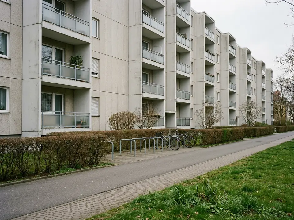 Többszintes panelházak sora balkonokkal, sétánnyal és alacsony sövénnyel